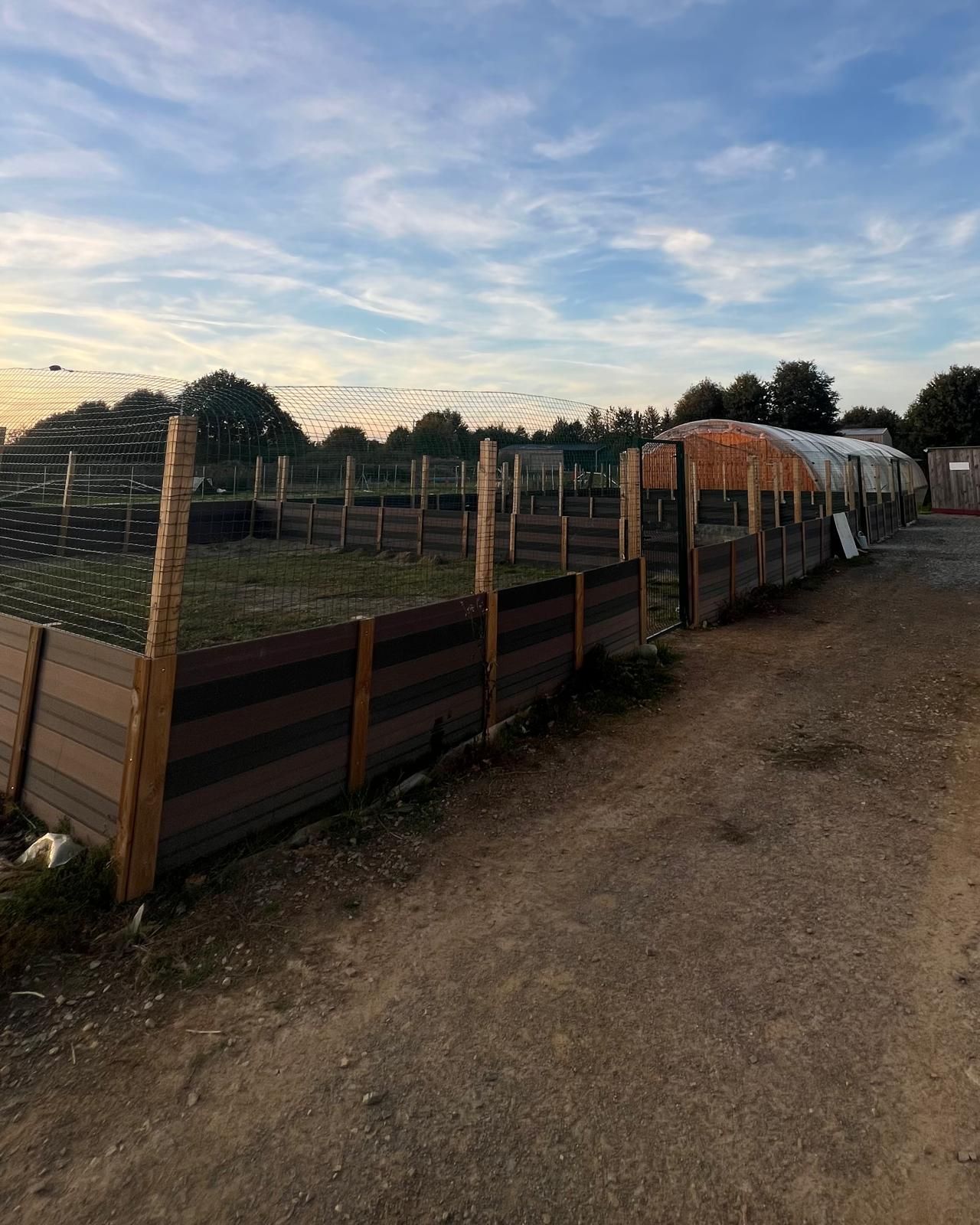 Des plates-bandes clôturées brunes à côté de serres sous un ciel nuageux.