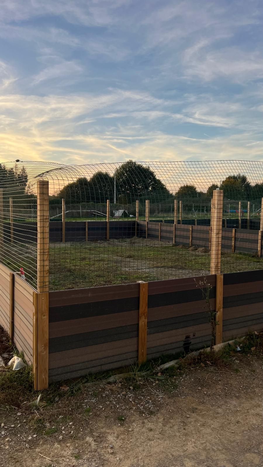 Une enceinte clôturée avec du bois et un filet, sur fond de ciel couchant.