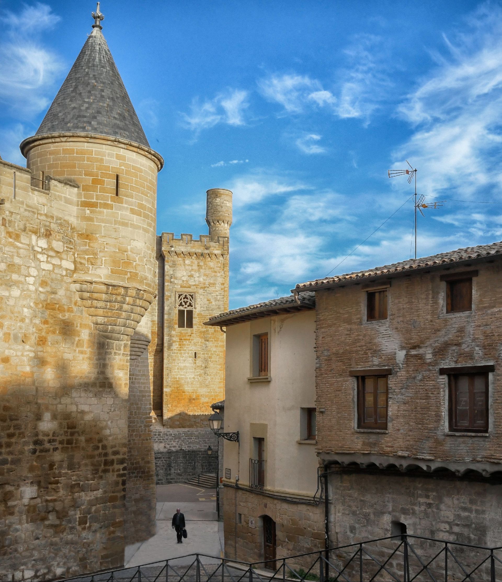 Torre de piedra y calle de pueblo histórico con edificios de color tostado bajo un cielo azul