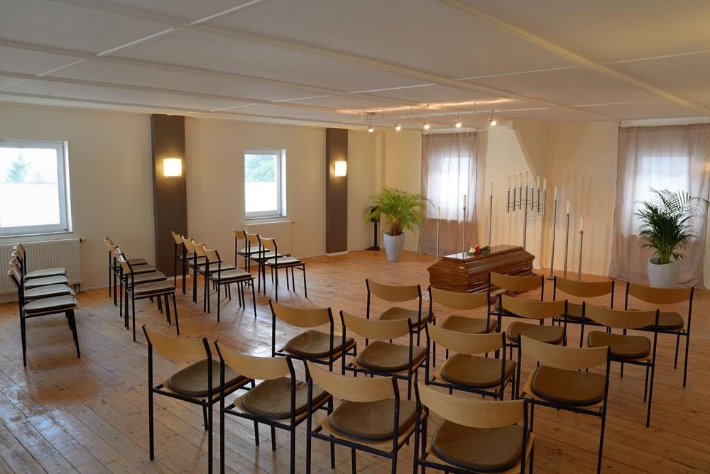 Stuhlreihen in einem Raum mit einem Sarg im Hintergrund