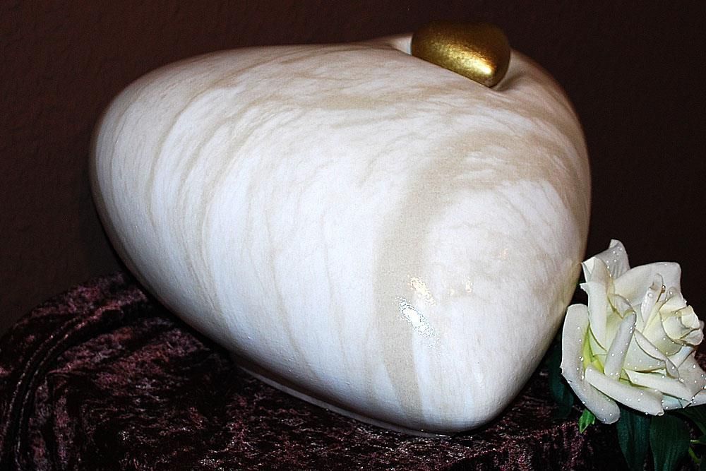 Eine weiße herzförmige Urne steht neben einer weißen Rose