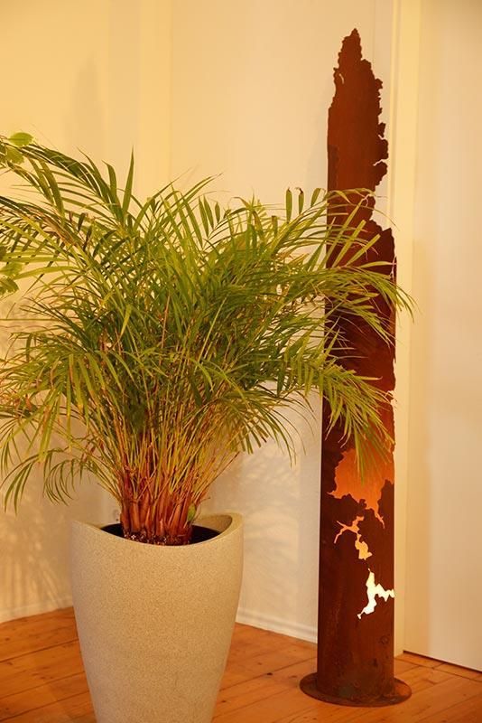 Eine Topfpflanze steht neben einer Skulptur auf einem Holzboden.