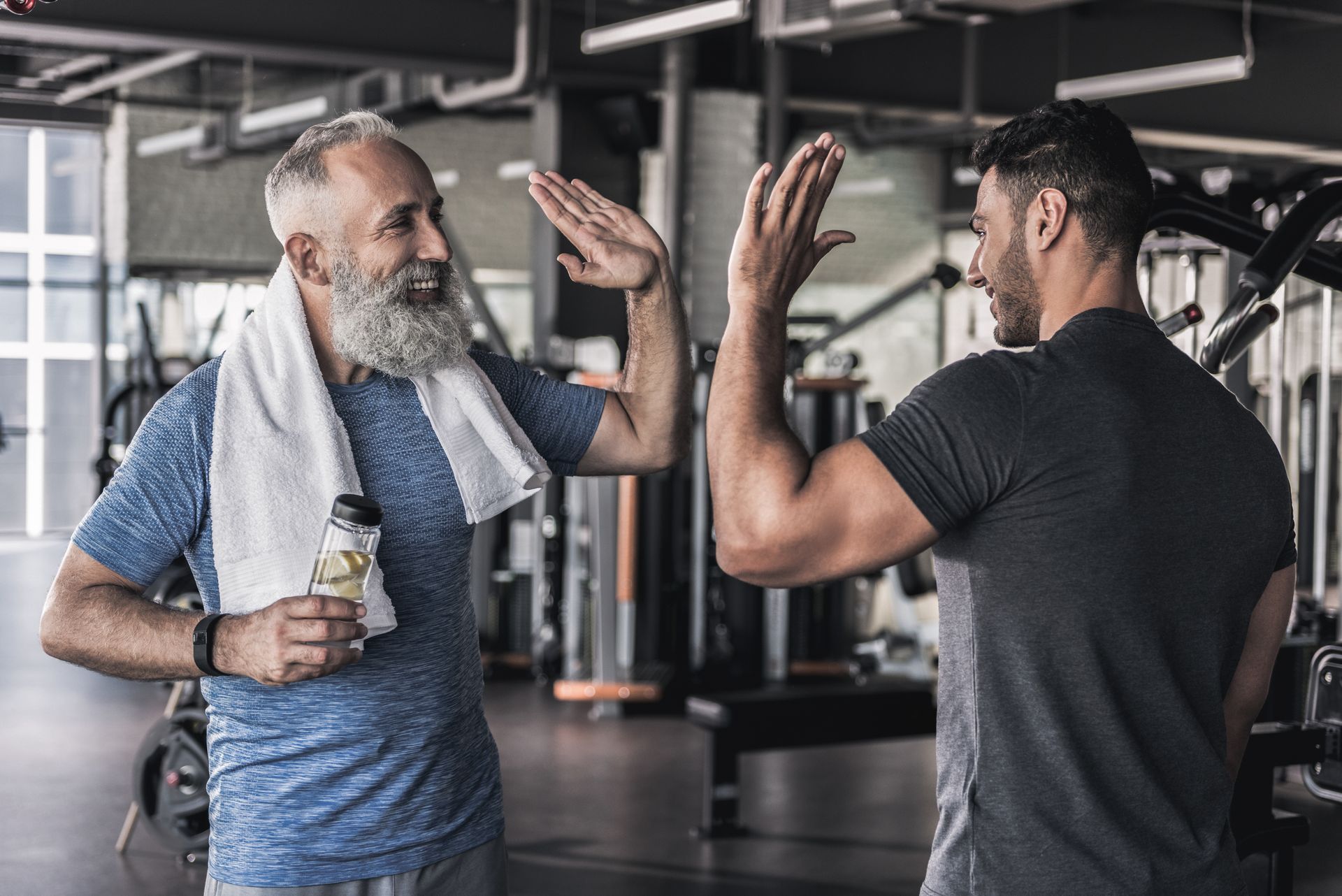 Deux hommes dans une salle de sport qui se tapent dans la main, l’un tenant une bouteille d’eau