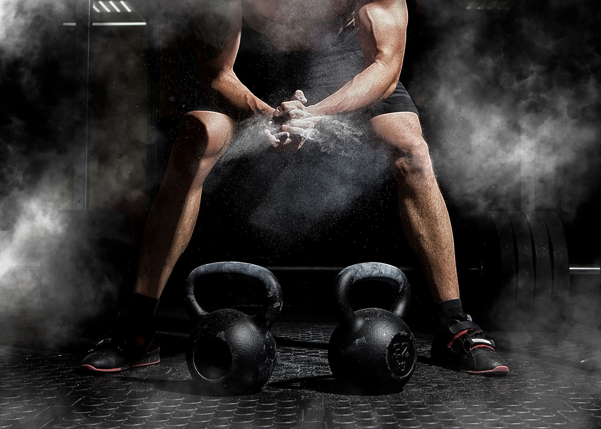 Un athlète se repose entre deux levées de kettlebell, de la poudre de magnésie dans une salle de sport sombre.