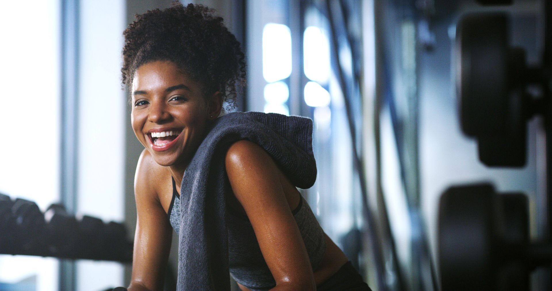 Femme souriante qui se repose avec une serviette après une séance d’entraînement dans une salle de sport