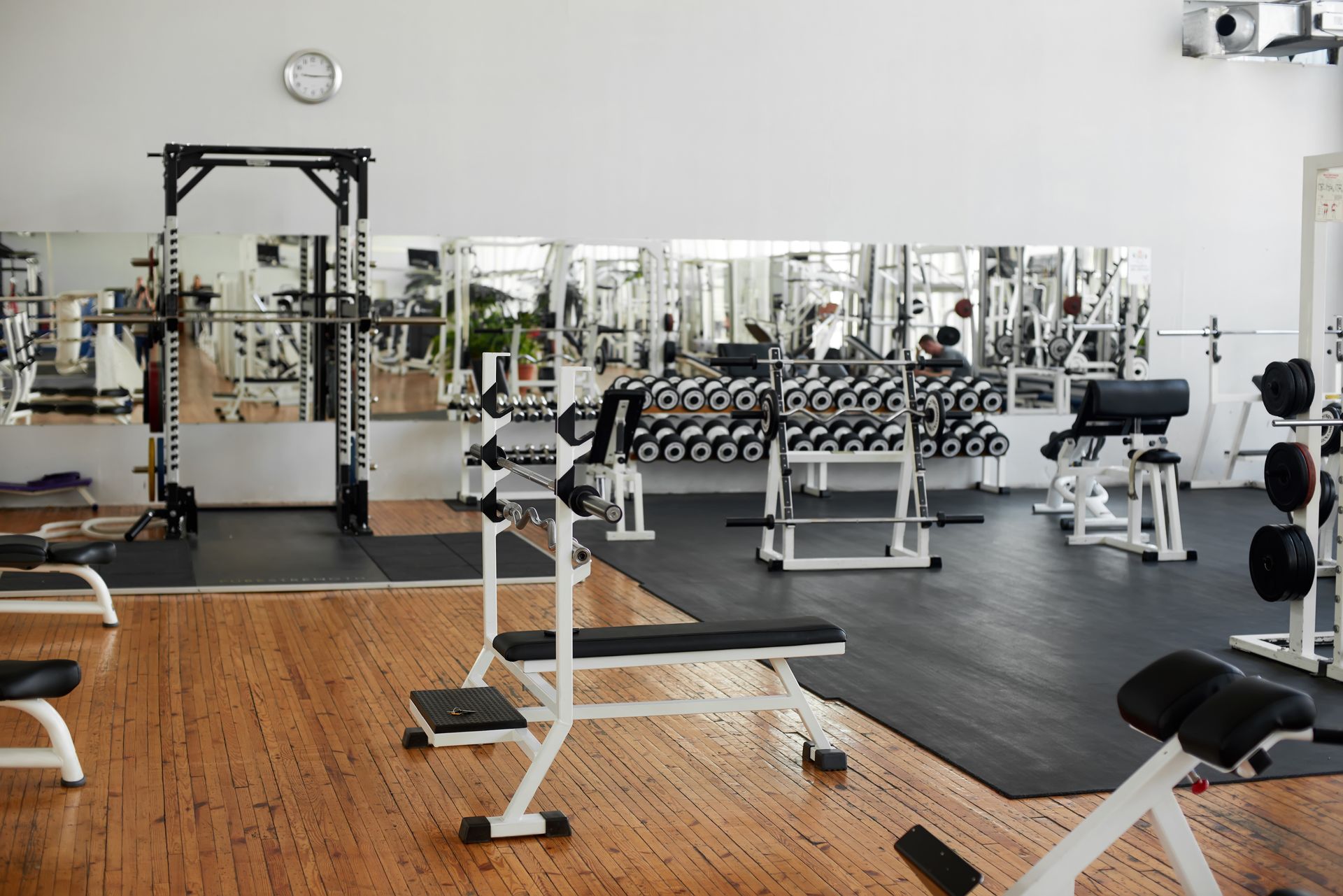 Salle de sport spacieuse avec des appareils de musculation, des miroirs, des haltères et un sol en bois et en caoutchouc