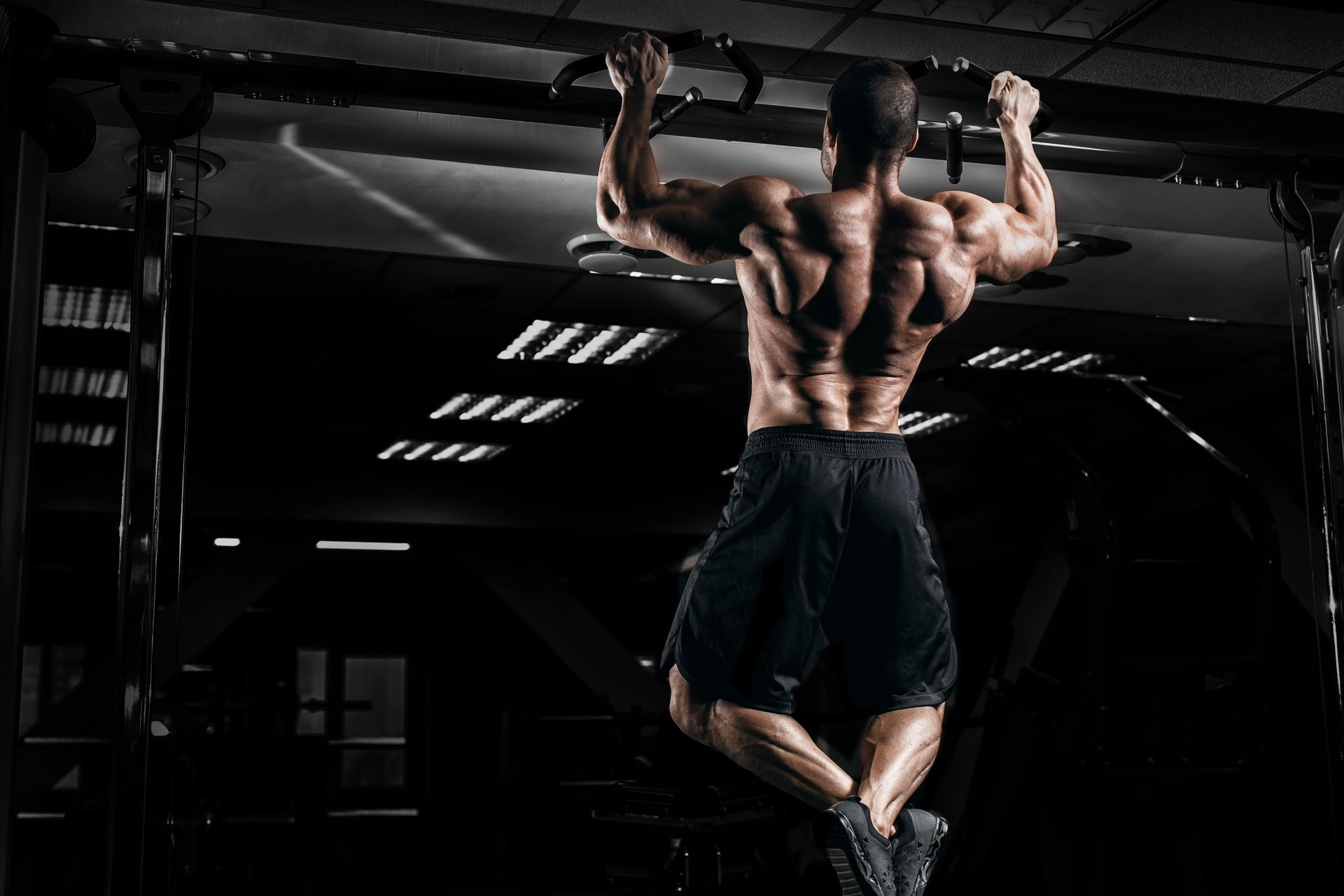 Un homme musclé fait une traction dans une salle de sport sombre