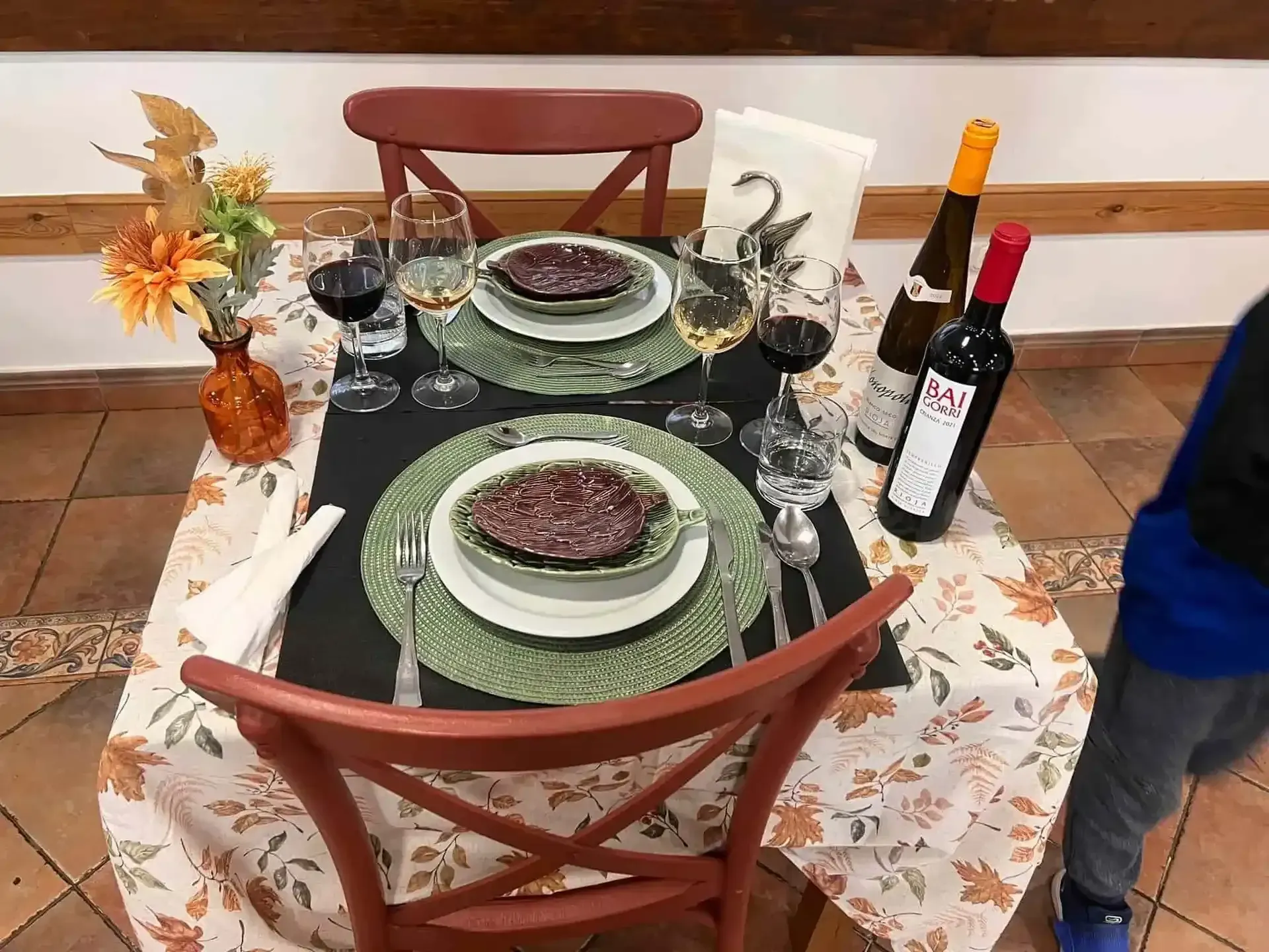 Mesa puesta para dos con comida, vino y decoraciones florales.