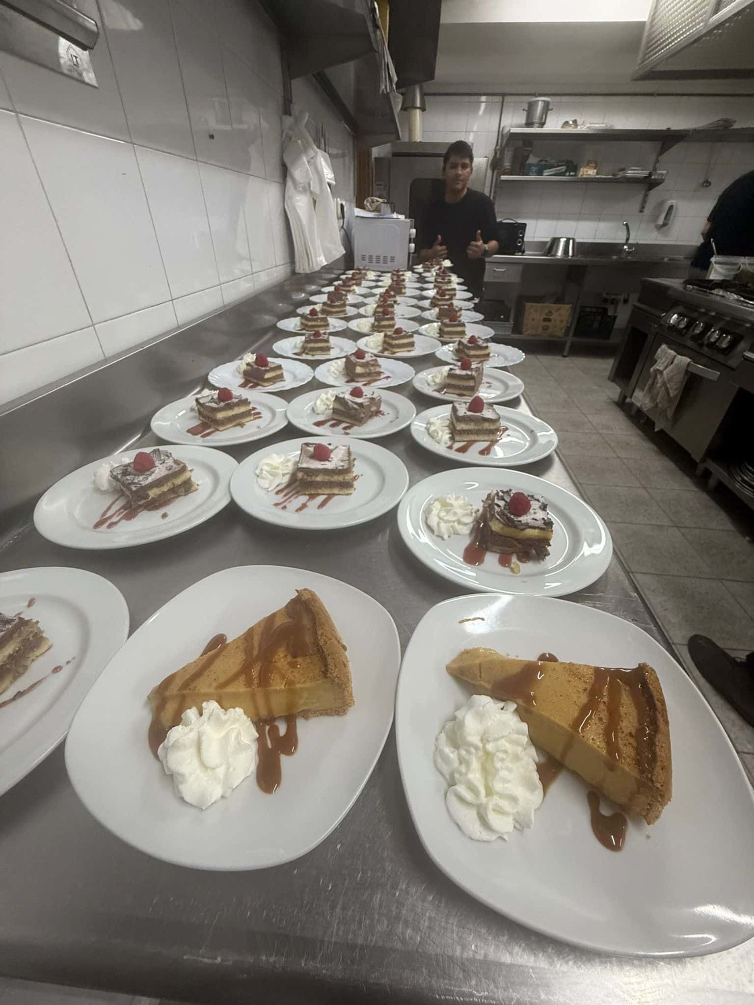 Postres servidos en un mostrador en una cocina comercial; un chef en el fondo.