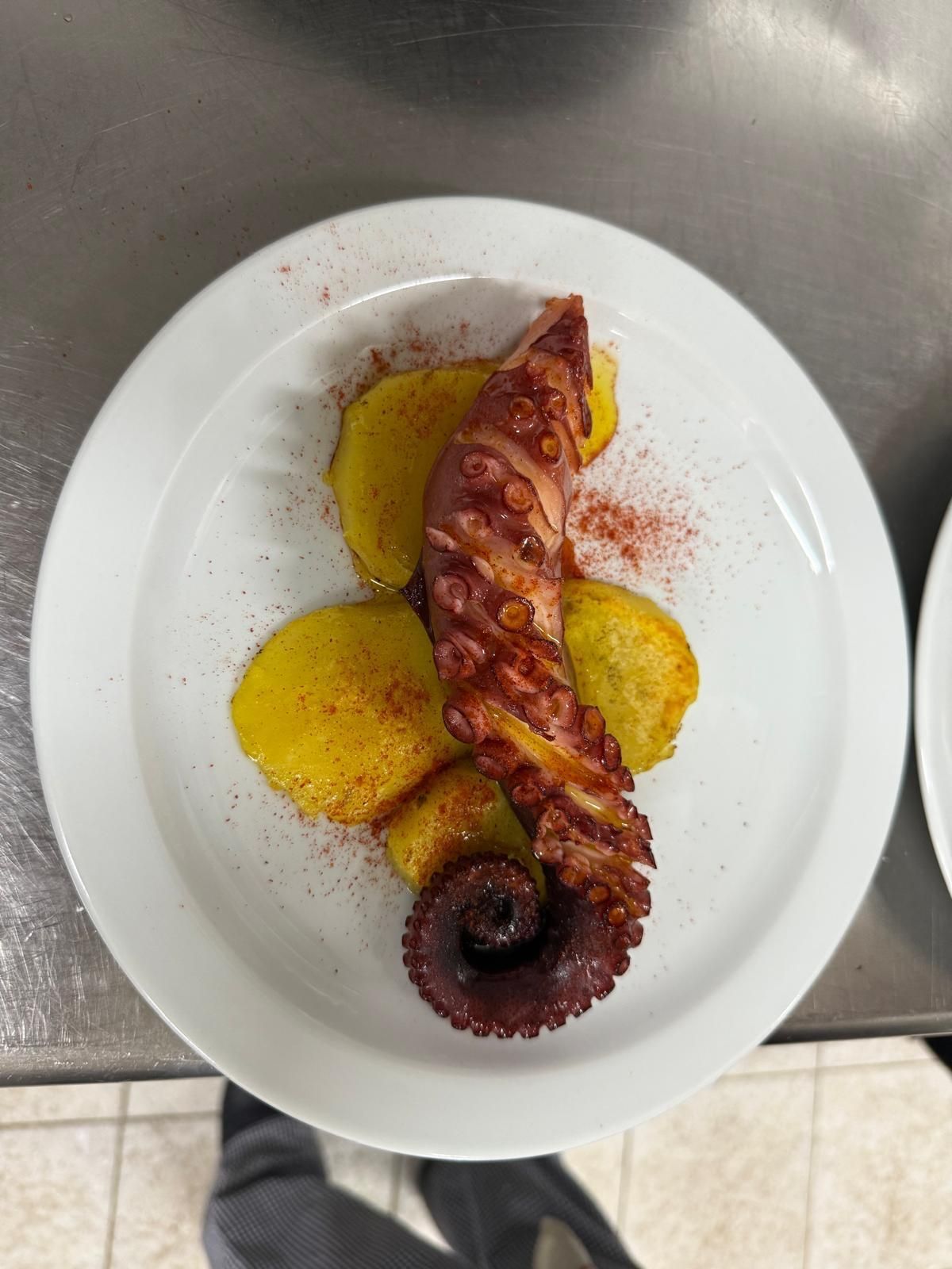 Tentáculo de pulpo a la parrilla sobre patatas doradas, espolvoreado con pimentón, en un plato blanco.