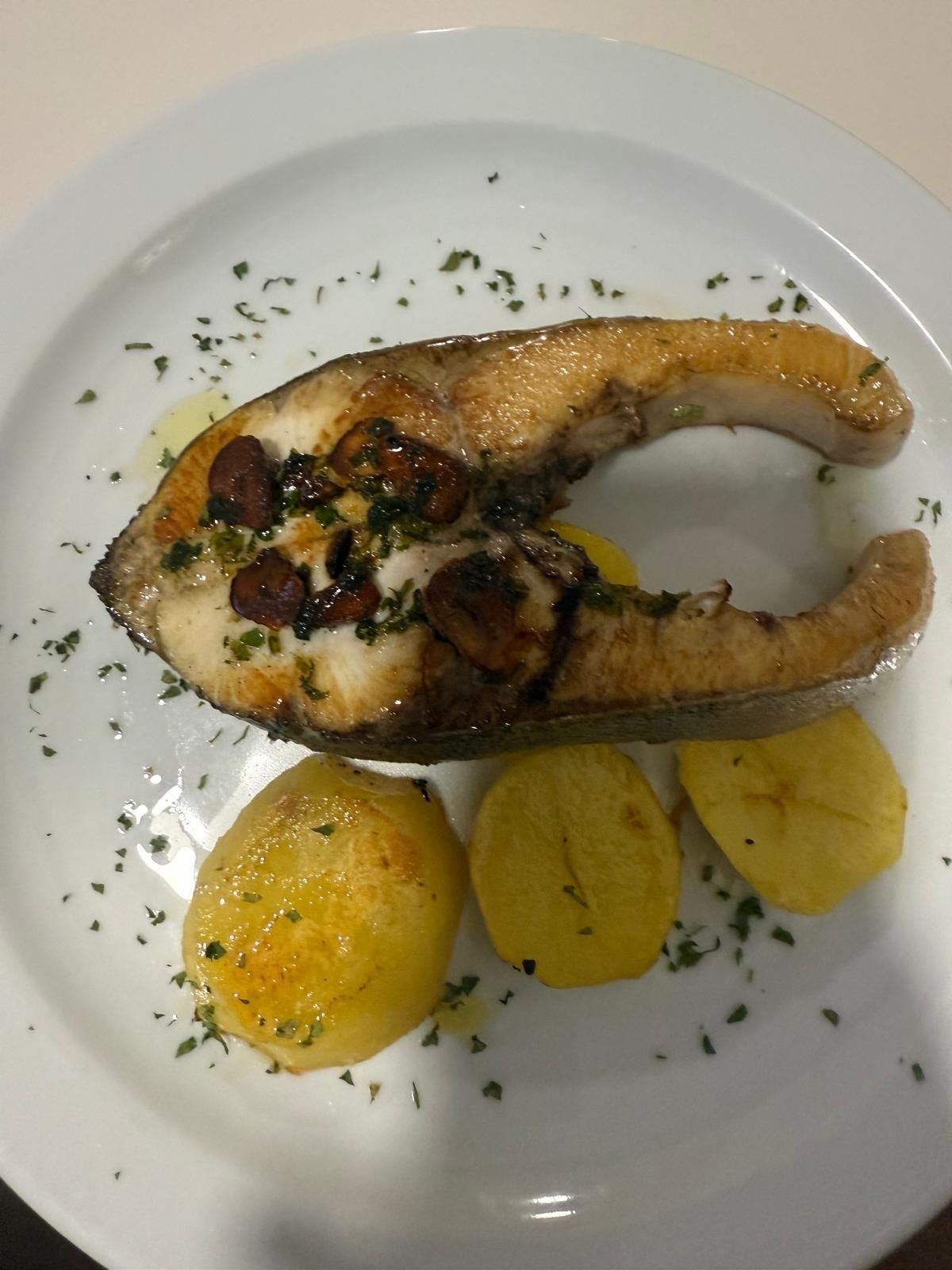 Filete de pescado a la parrilla con patatas, adornado con hierbas en un plato blanco.