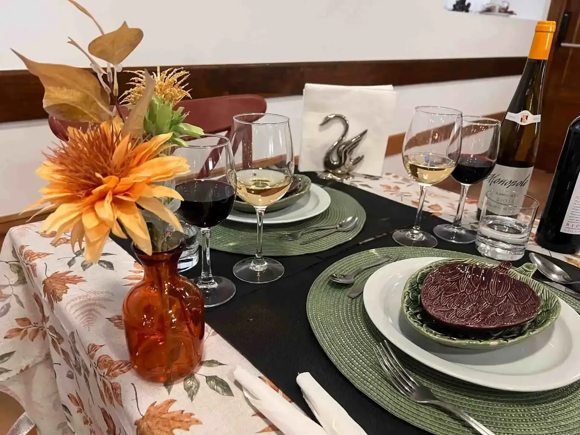 Mesa formal con copas de vino, centro de mesa floral y platos sobre manteles individuales verdes.