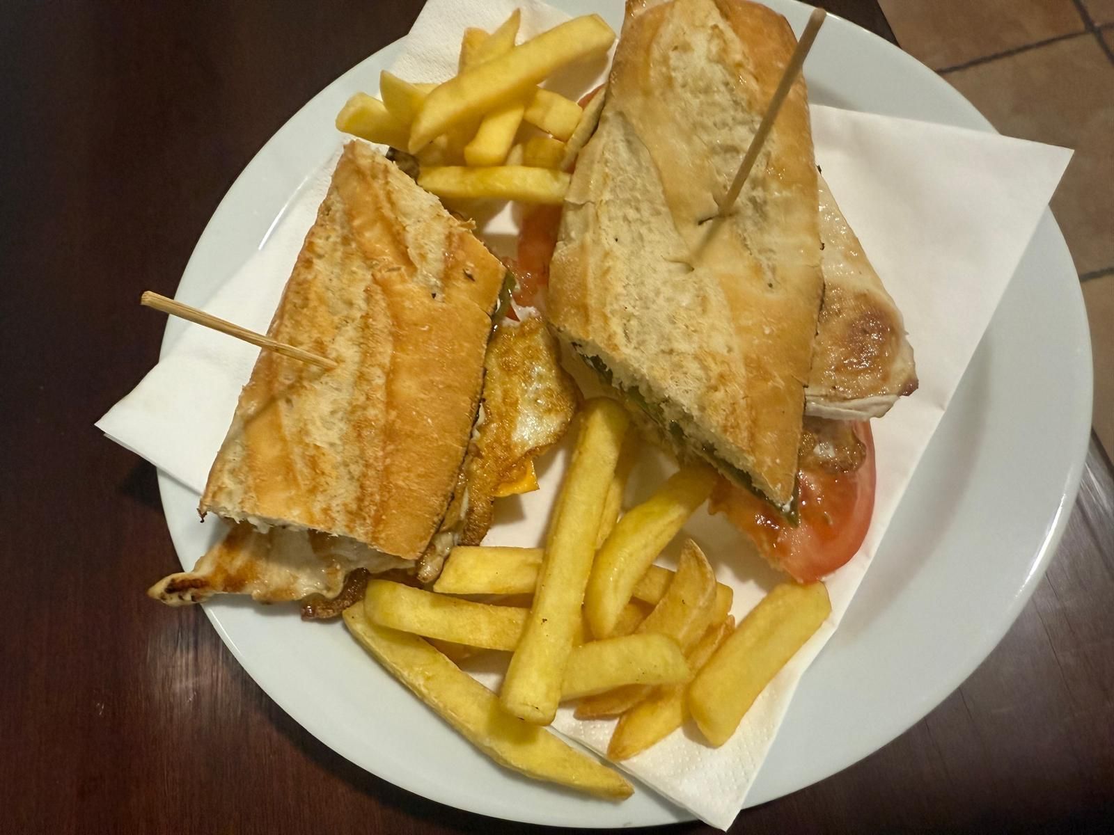 Sándwich cortado a la mitad con patatas fritas en un plato.