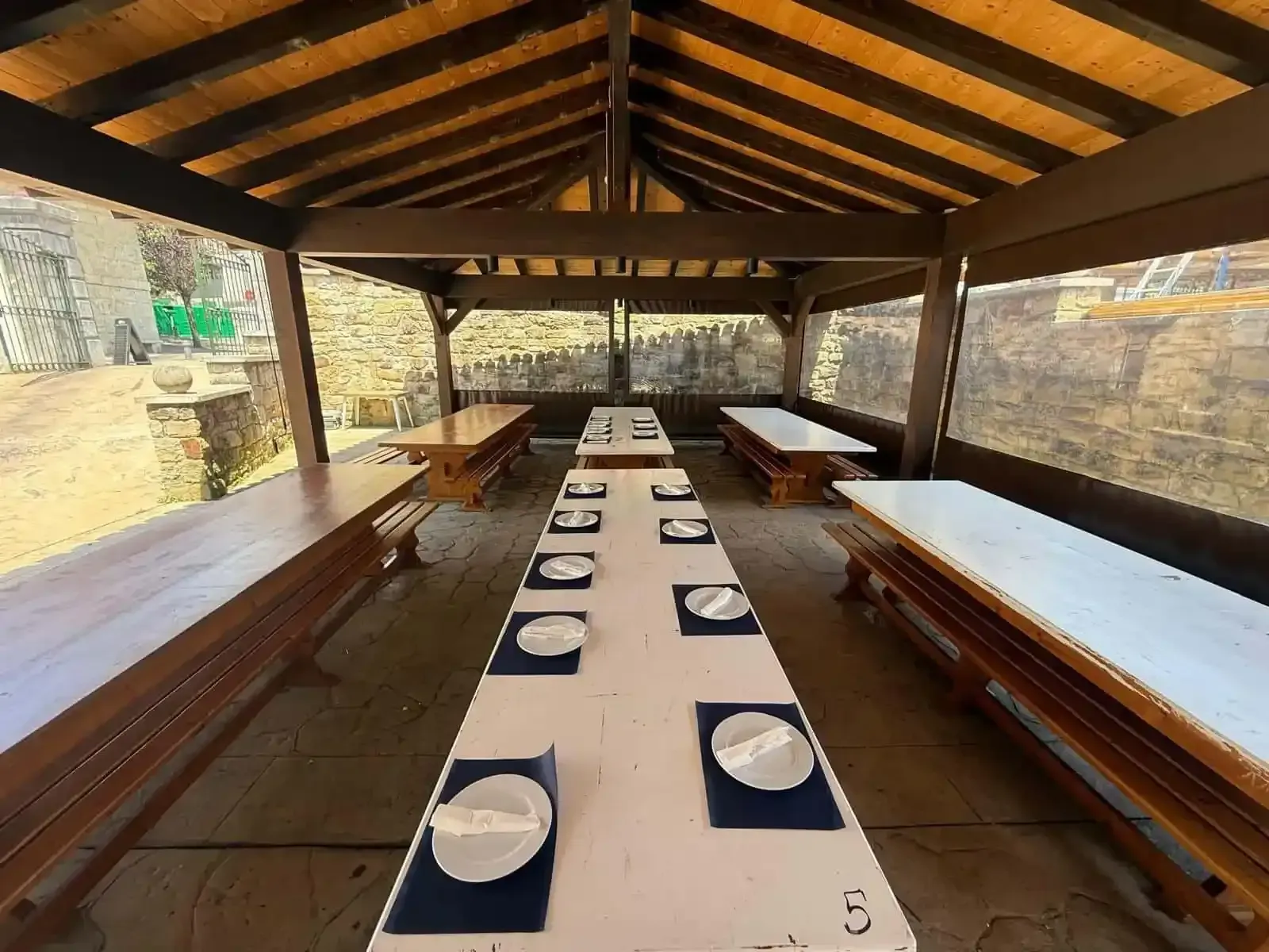 Zona de comedor exterior cubierta con mesas largas preparadas para comer.