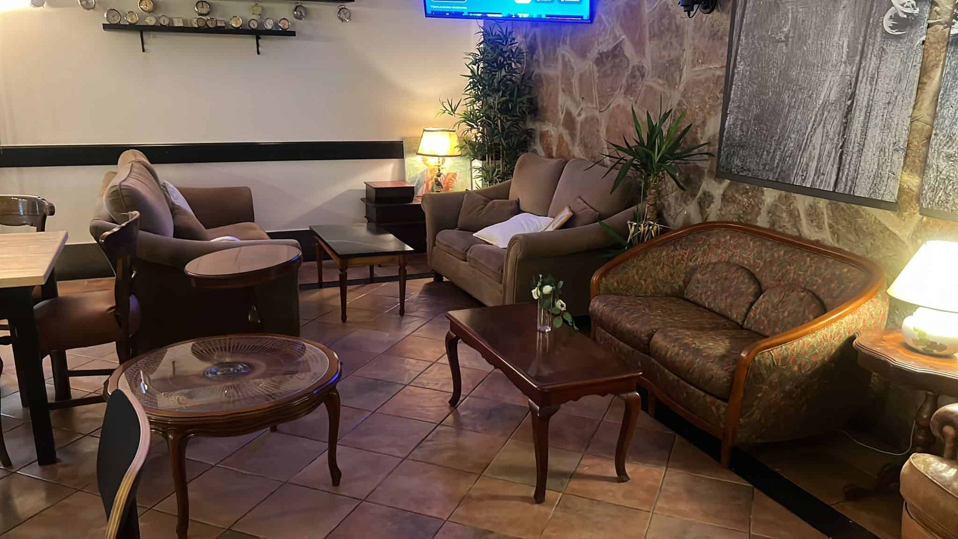 Acogedora sala de estar con sofás, mesas pequeñas y lámparas, frente a paredes de piedra y madera.