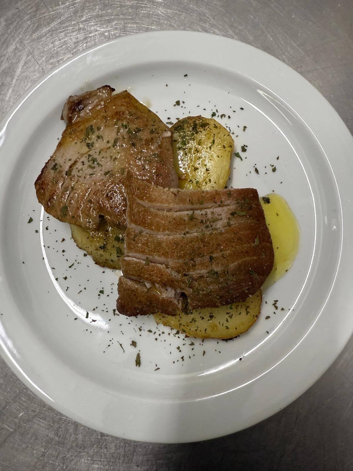 Filete de atún a la parrilla con patatas asadas, adornado con hierbas en un plato blanco.