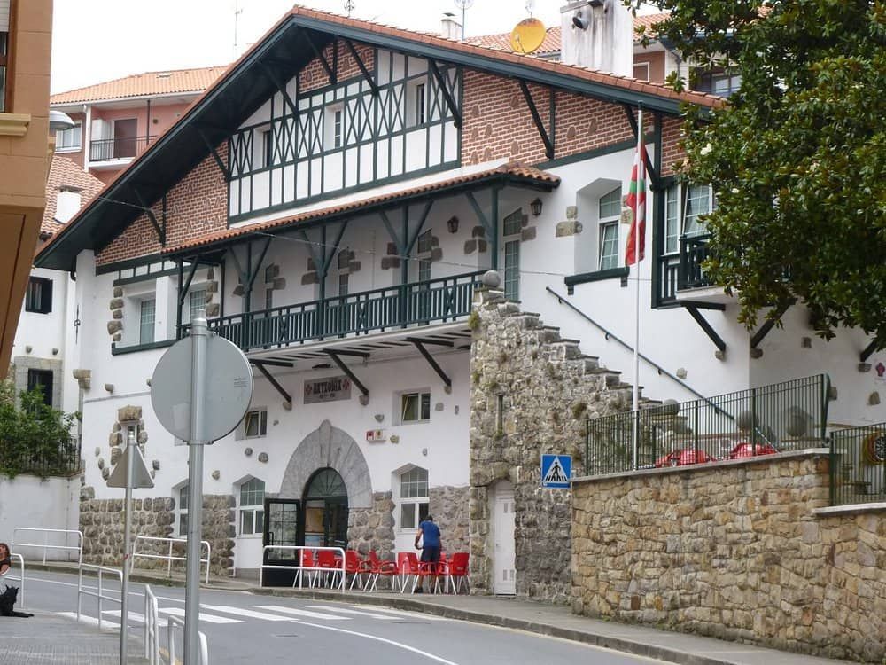 Edificio con fachada de piedra y madera, balcón, bandera vasca, calle.