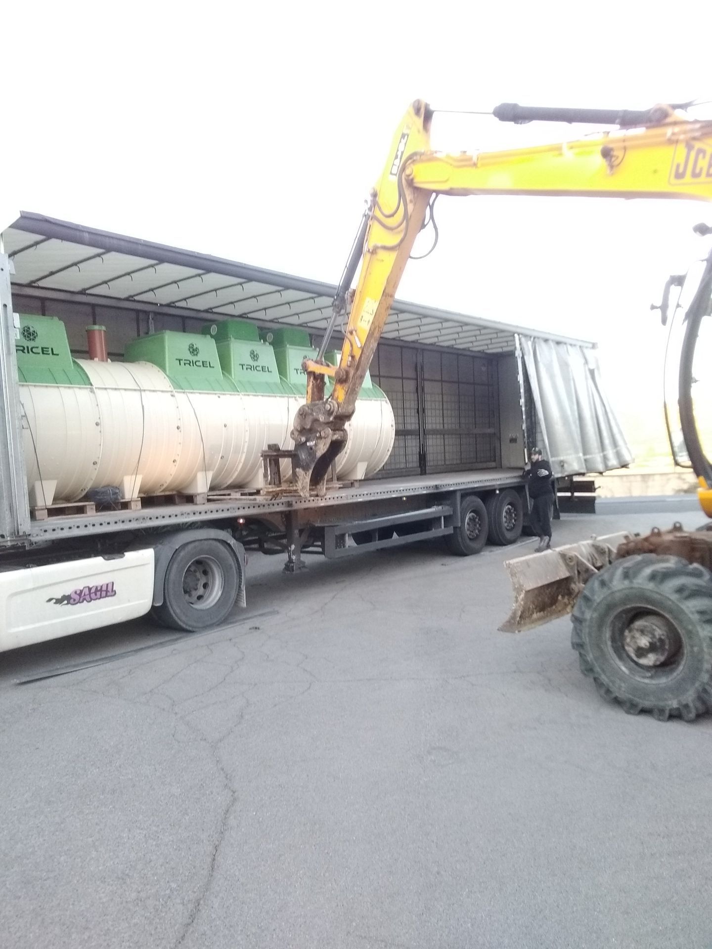 Une pelle mécanique jaune charge des réservoirs cylindriques dans une semi-remorque.