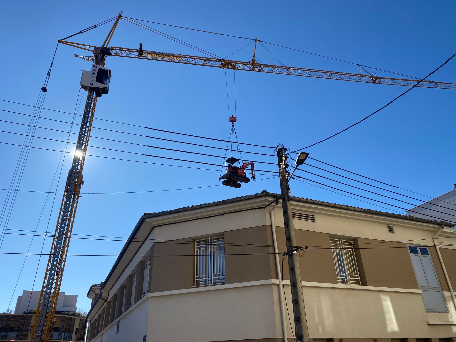 Par une journée ensoleillée, une grue de chantier soulève des engins de chantier près d'un bâtiment.