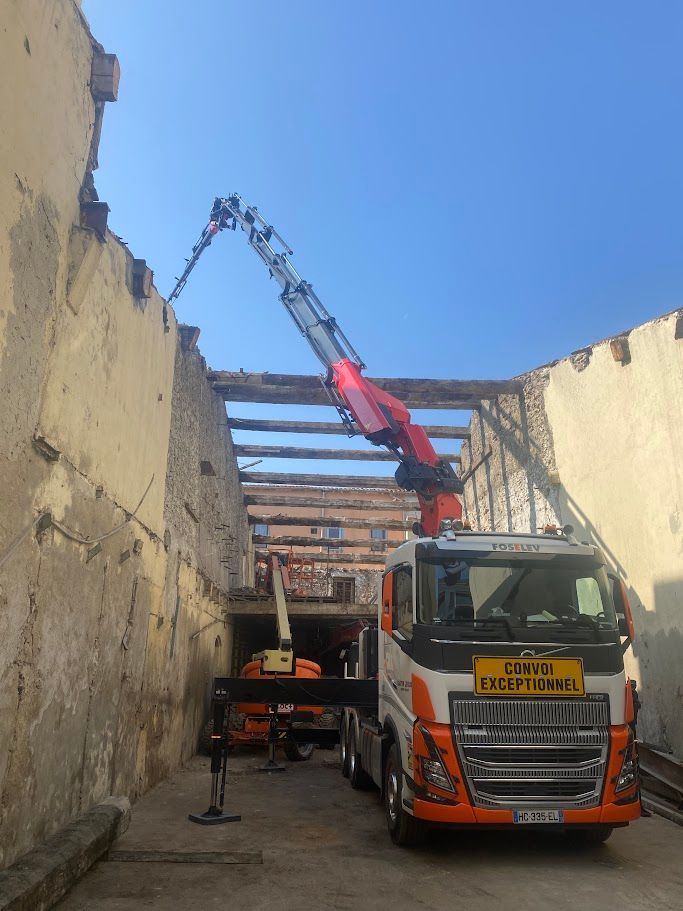 Camion-grue en train de démanteler le toit d'un immeuble, sous un ciel bleu dégagé.