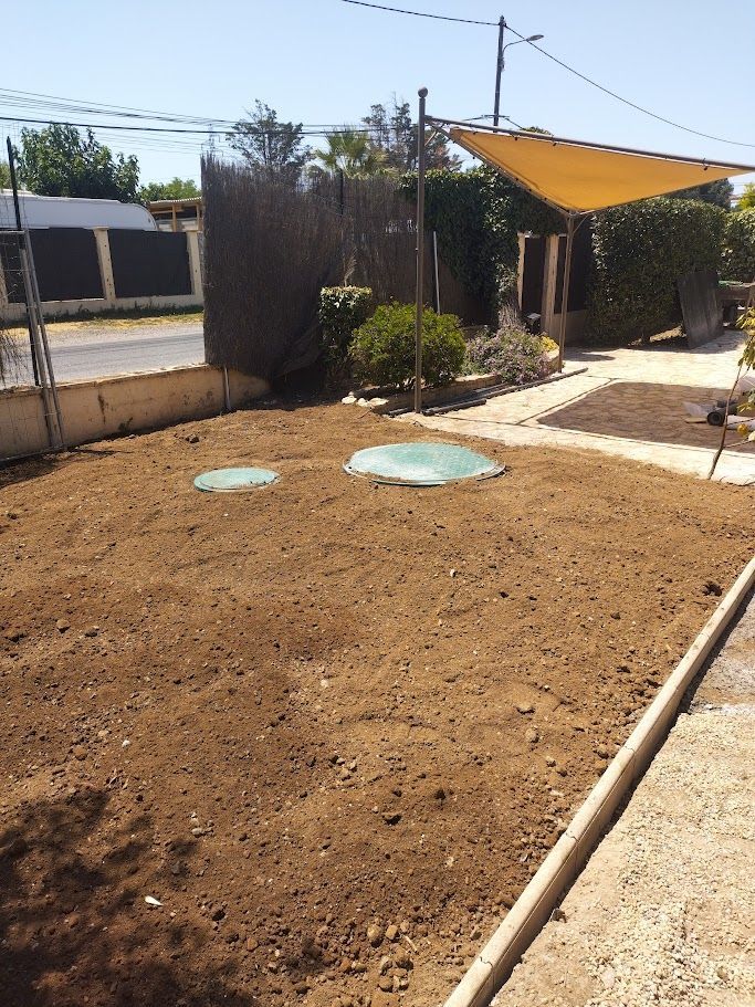 Un parterre de jardin fraîchement labouré, agrémenté de deux couvertures circulaires, bordé d'un chemin et d'une clôture en béton, sous un auvent.