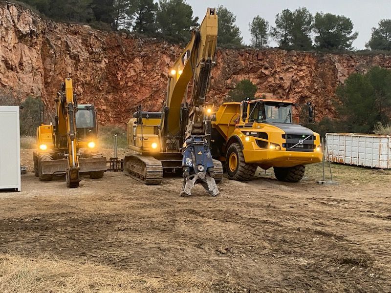 Trois engins de chantier jaunes stationnés dans une carrière : une excavatrice, une pelle rétro et un camion-benne.