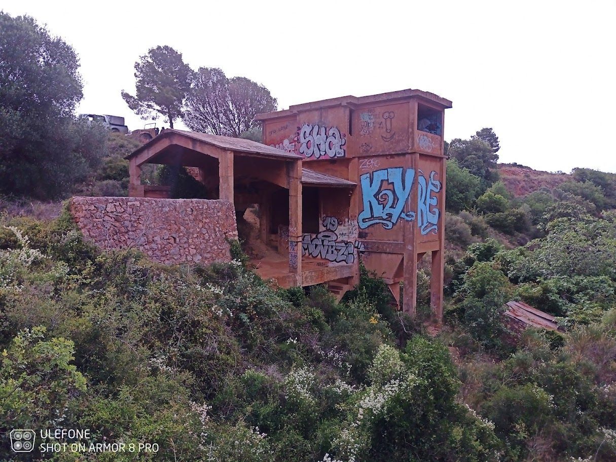 Bâtiment en béton abandonné et couvert de graffitis, situé dans une zone boisée et doté d'une entrée couverte.