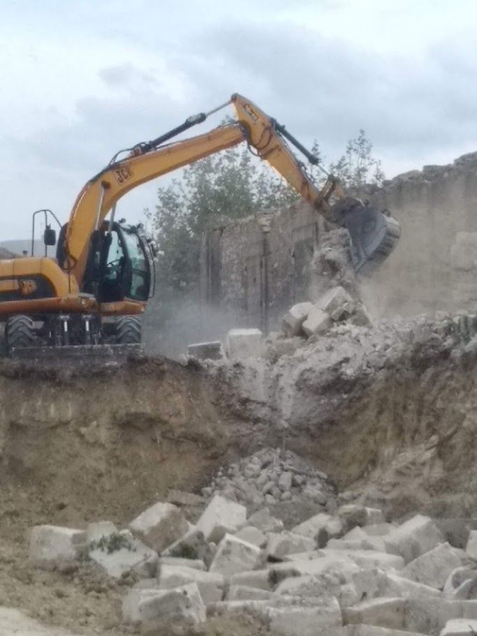 Une pelleteuse jaune démolit des blocs de béton sur un chantier de construction.