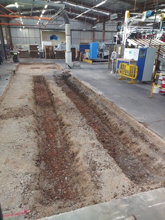 Une pelleteuse jaune creuse une tranchée dans un champ avec de l'herbe par une journée ensoleillée.