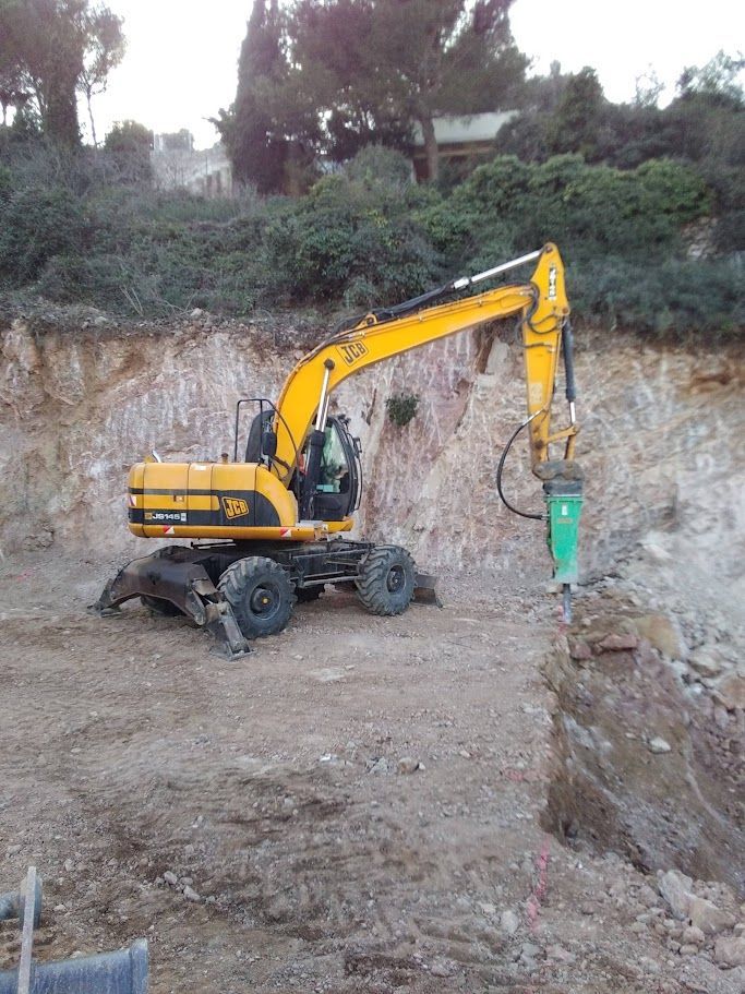 Une pelleteuse jaune creuse la terre près d'une maison par une journée ensoleillée.