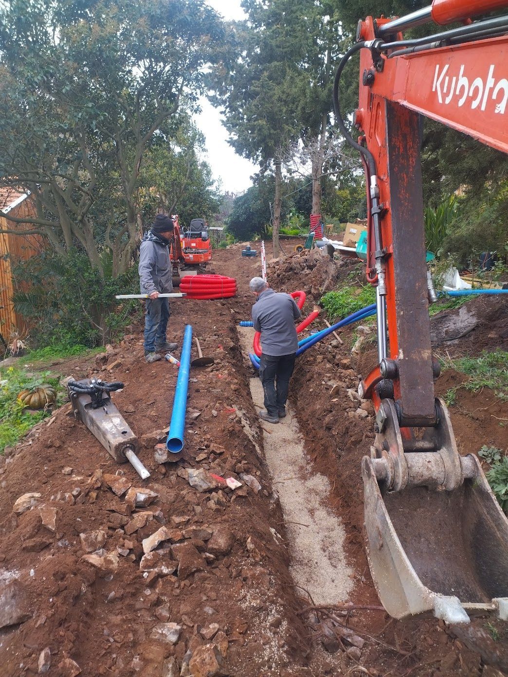 Une pelleteuse jaune creuse la terre près d'une maison par une journée ensoleillée.
