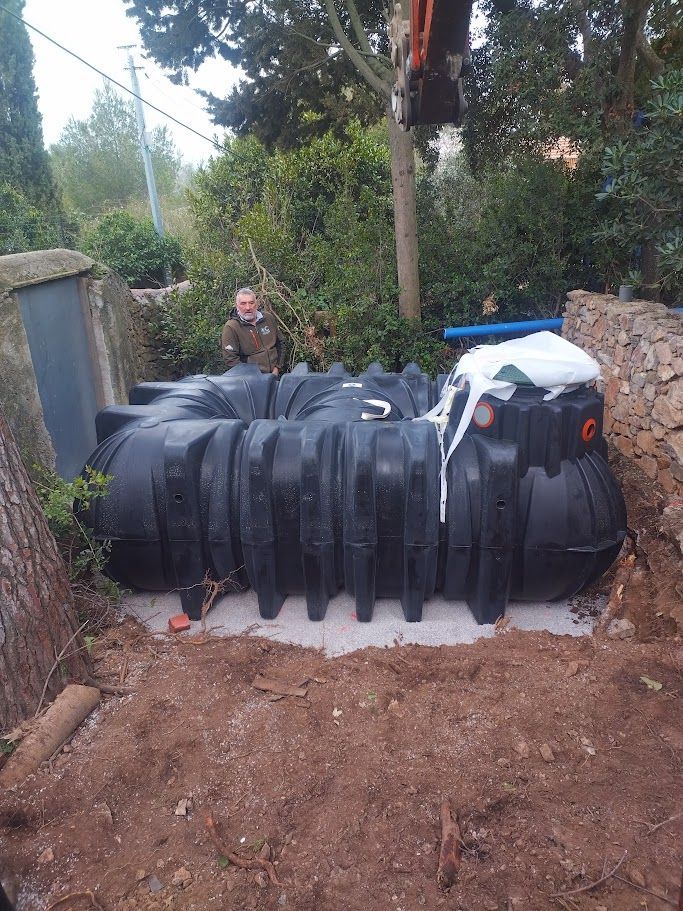 Une fosse septique noire est installée dans une fosse à terre préparée, un ouvrier se tenant à proximité.