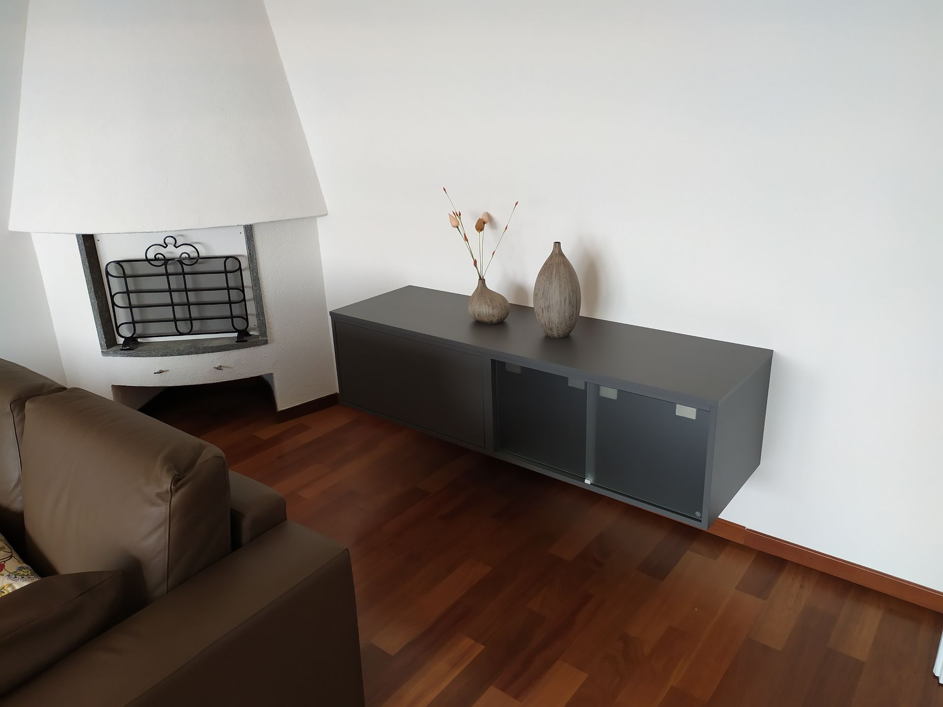 Arredamento per la sala. Esecuzione su misura. Colore grigio antracite. Vetri di sicurezza satinati bianchi. Piani di lavoro. Fissaggio alle pareti con attaccaglie nascoste e regolabili. 5 elementi con doppie antine scorrevoli in vetro. 1 elemento a ribalta per TV. 1 elemento a vista.