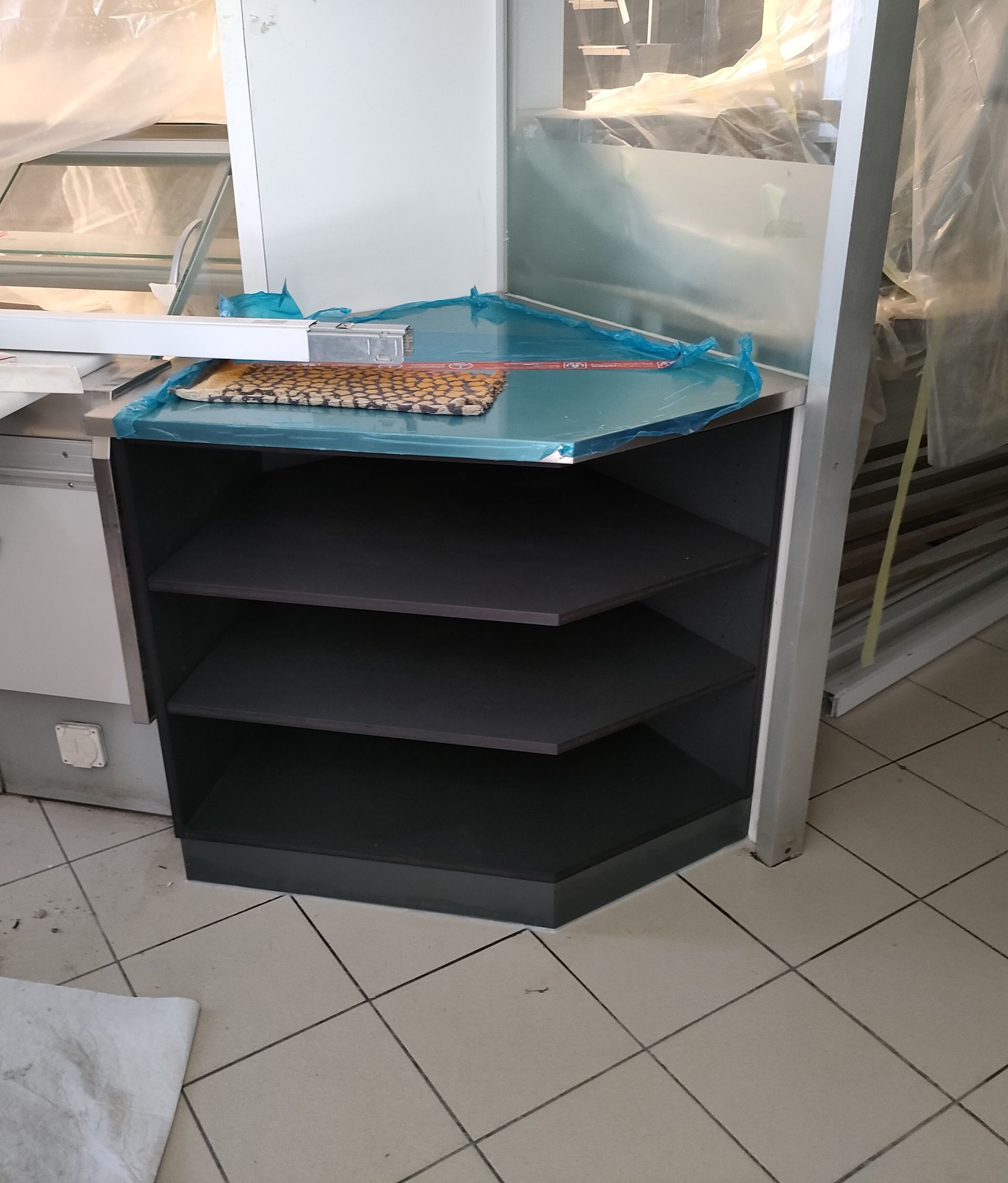 Arredamento negozio. Mobile d'angolo. Esecuzione su misura con materiale Swiss Krono - SwissCDF grigio U164 PE, resistente all'umidità, spessore 19.4 mm. Parti interne a vista con 2 ripiani. 
Zoccolo con parti frontali chiuse.
Rivestimento piano superiore in acciaio inox con risvolti.
