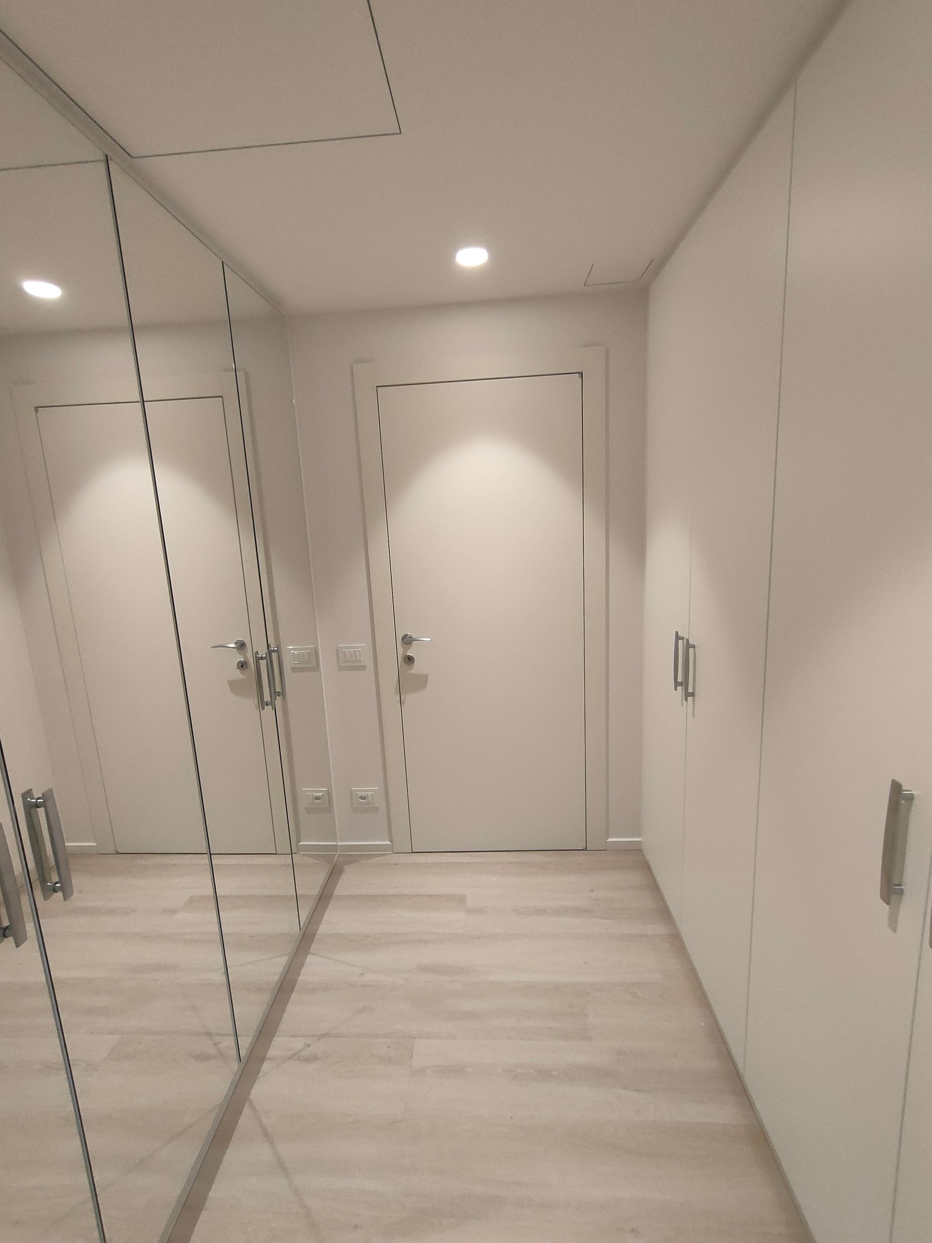 armadi a muro su 2 lati del locale. Un lato 4 ante laccate bianco RAL 9016, lato  opposto ante laccate con 4 specchi. Cerniere nascoste con chiusura ammortizzata. Luci led incassate con sensore di movimento. Maniglie Colombo