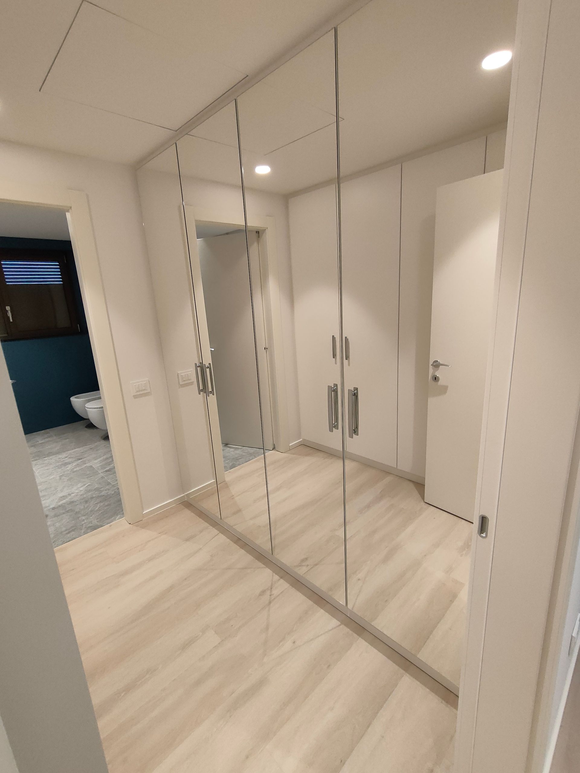 armadi a muro su 2 lati del locale. Un lato 4 ante laccate bianco RAL 9016, lato  opposto ante laccate con 4 specchi. Cerniere nascoste con chiusura ammortizzata. Luci led incassate con sensore di movimento. Maniglie Colombo