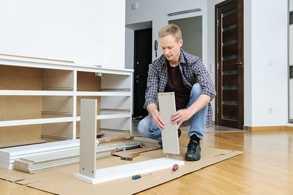 Dos trabajadores de mudanzas con monos azules llevan un sillón beige en una habitación luminosa con cajas.