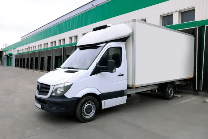Camión de caja blanca estacionado en un muelle de carga con molduras verdes.