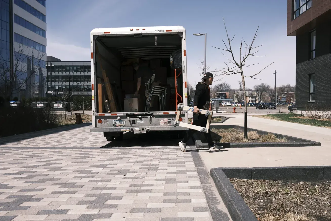 Dos trabajadores cargan un panel grande en la parte trasera de una camioneta blanca estacionada en un patio de ladrillos.