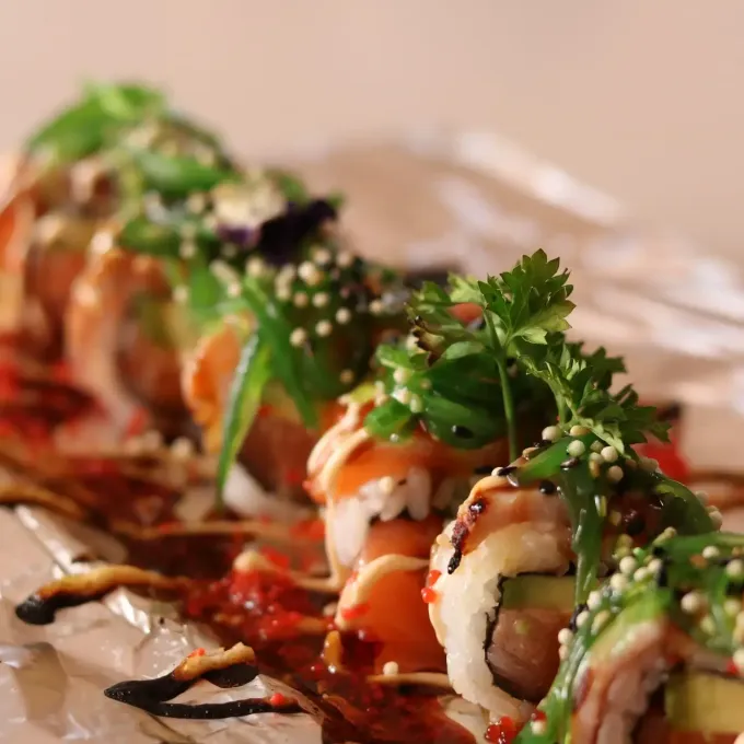 Rollos de sushi cubiertos con hierbas y semillas de sésamo, en un plato con un chorrito de salsa