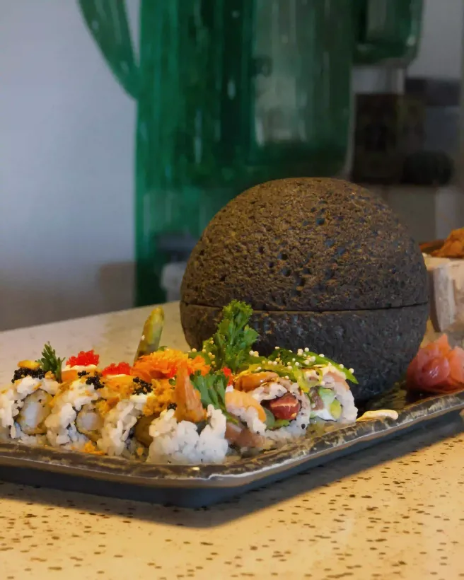 Bandeja de sushi con una variedad de rollos y una gran esfera de arroz negro sobre una mesa moteada