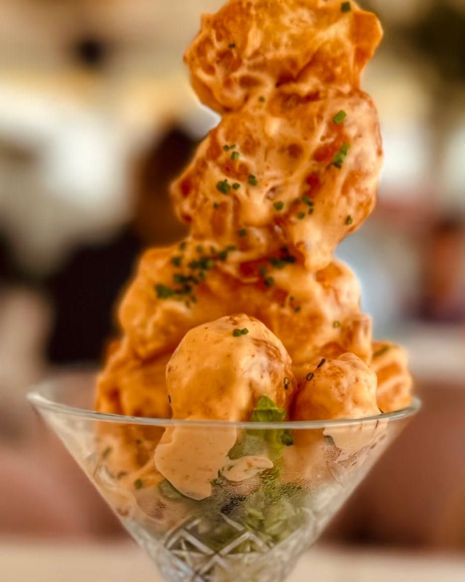 Bocados de pollo frito de color naranja apilados en una copa de martini y decorados con hierbas.