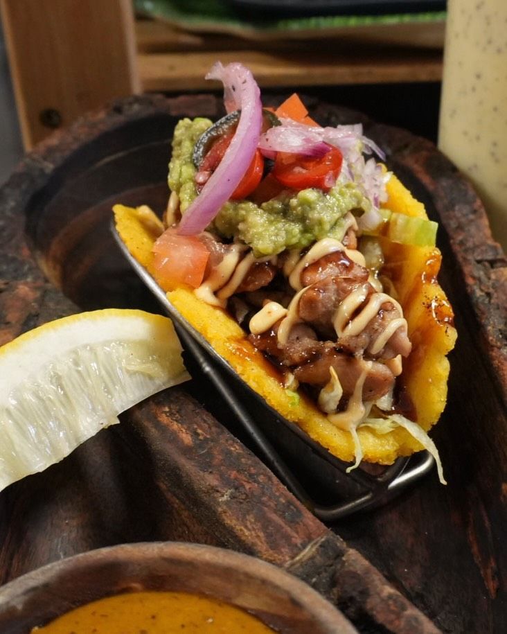 Taco en una sartén de hierro fundido con guacamole, cebolla, tomate y una rodaja de lima sobre una mesa rústica