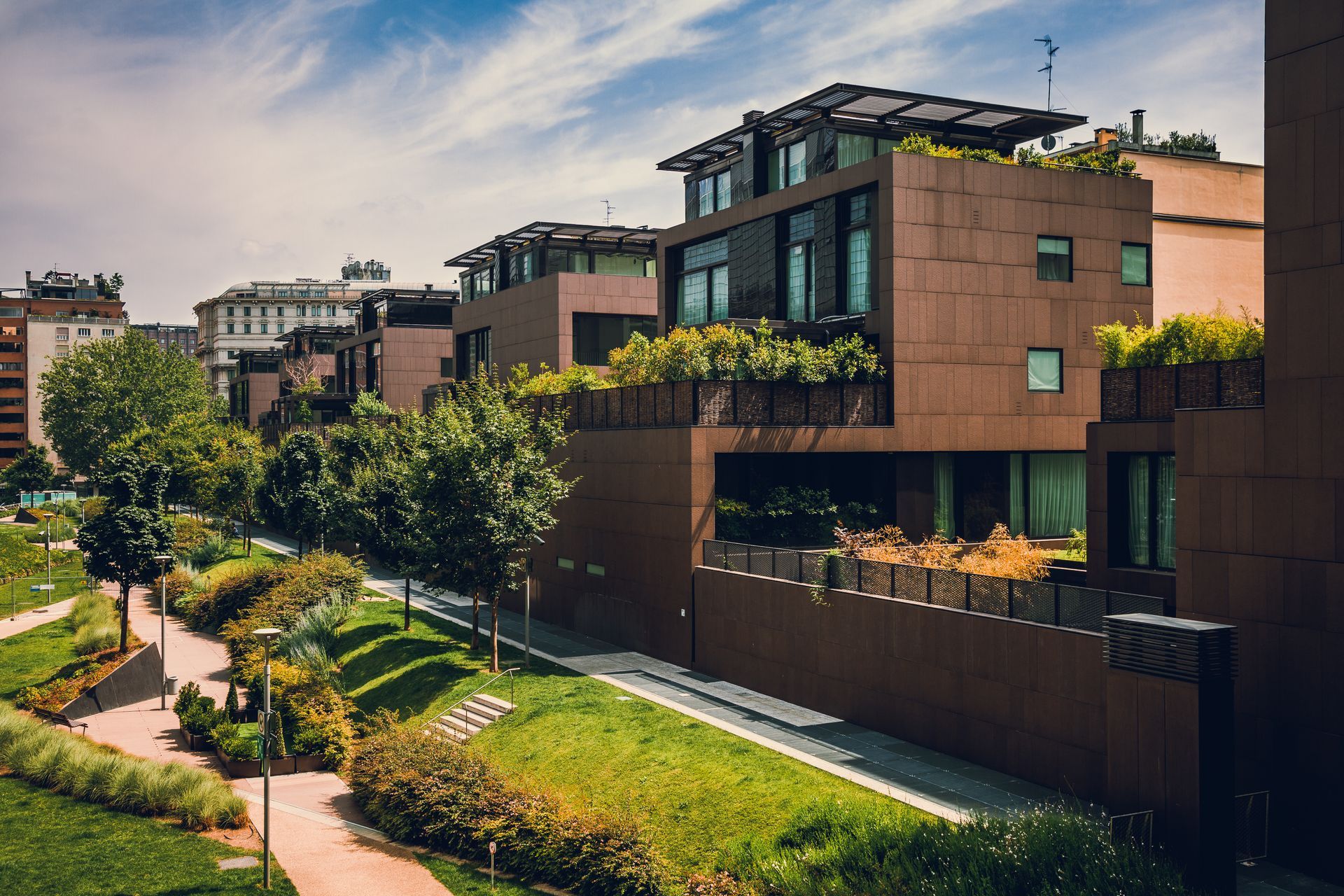 Edificios de apartamentos modernos con jardines en la azotea junto a un sendero arbolado al atardecer.
