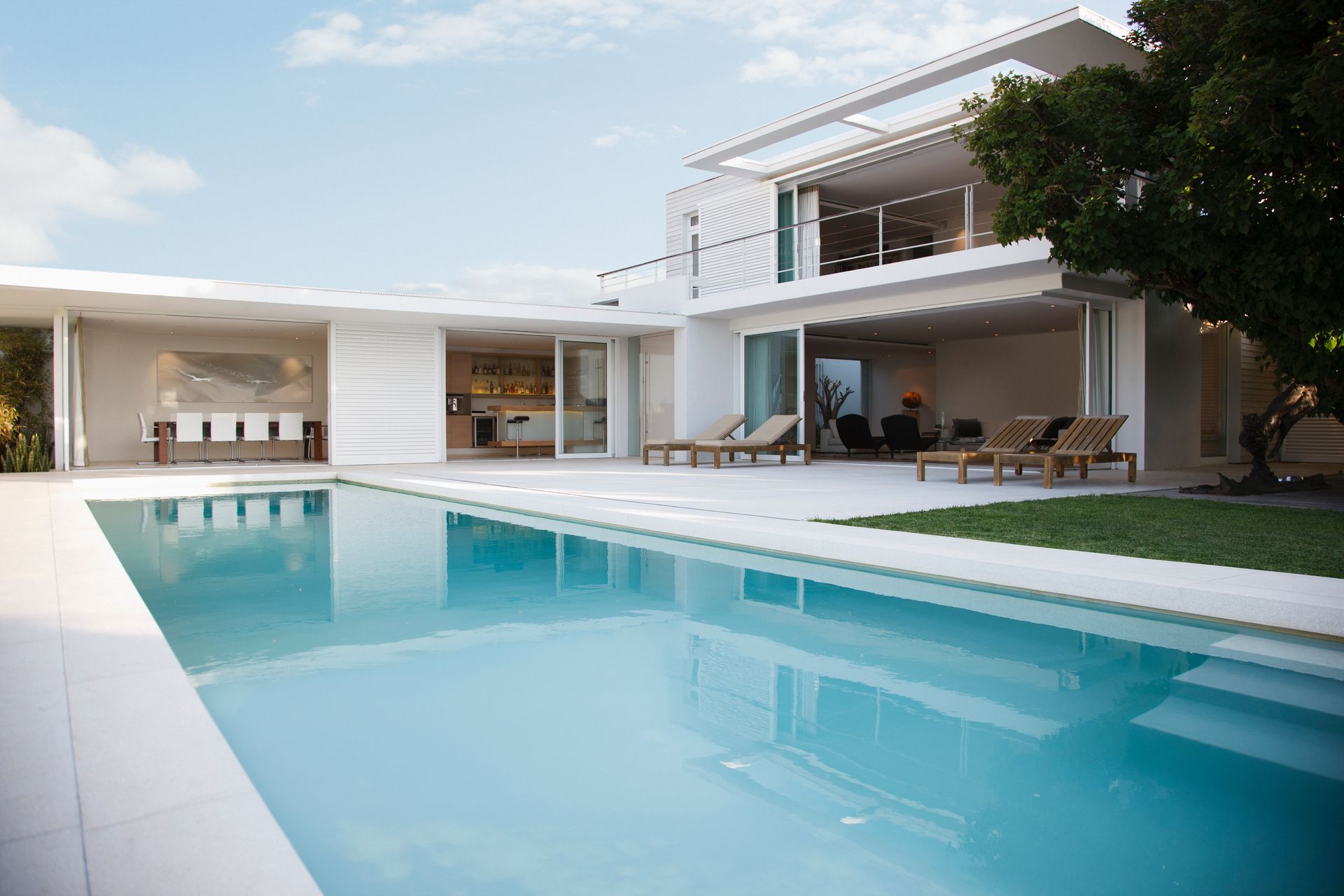 Villa blanca moderna con piscina turquesa y terraza con asientos bajo un cielo despejado.