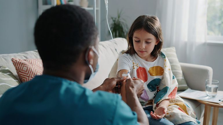 Un médecin met un pansement sur le bras d'une jeune fille assise sur un canapé.