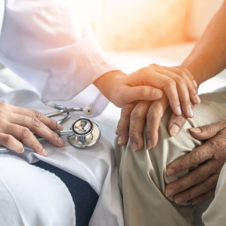 Un professionnel de santé réconforte un patient en lui tenant la main dans un cabinet lumineux.