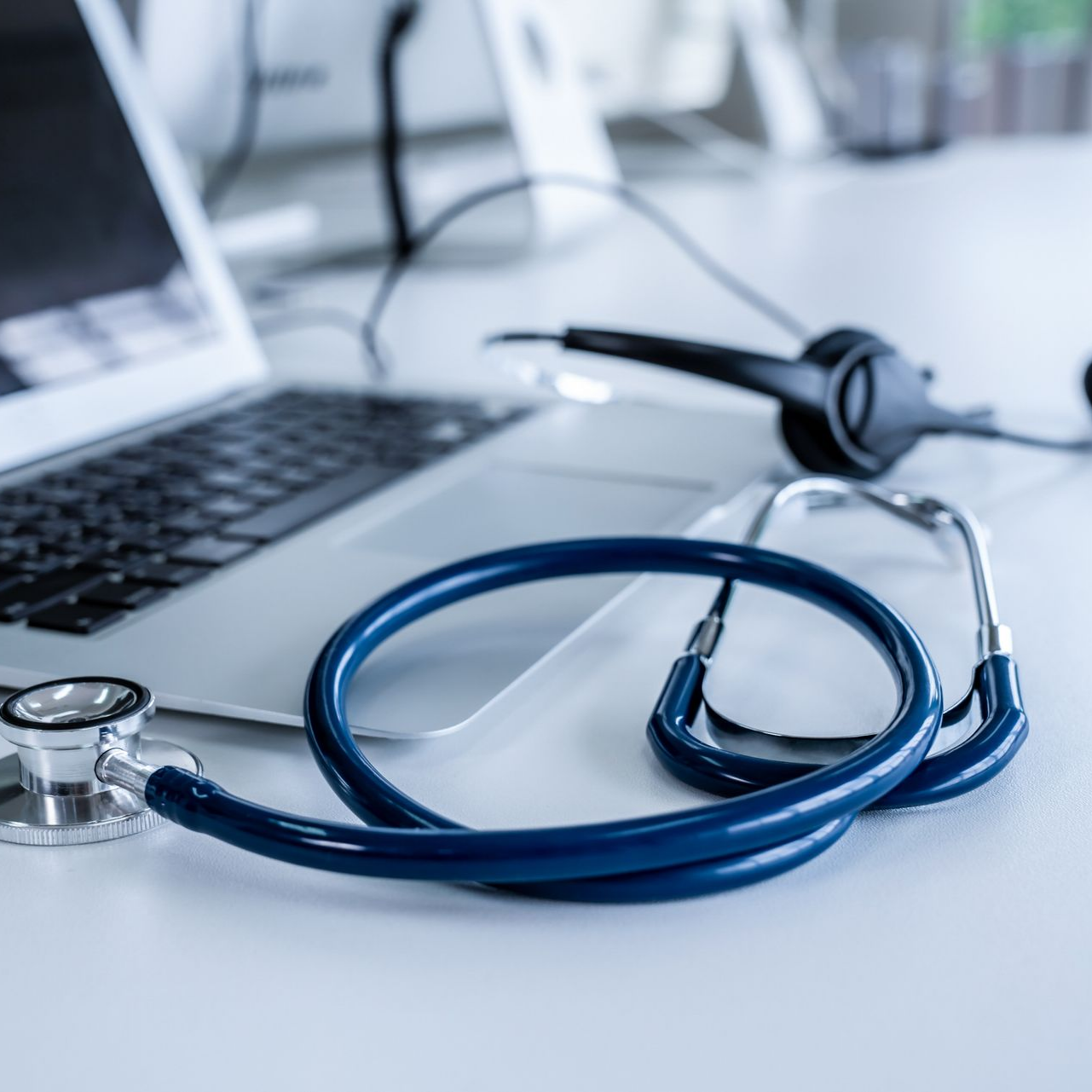 Ordinateur portable avec un stéthoscope bleu sur un bureau, évoquant la télémédecine ou une consultation médicale en ligne.