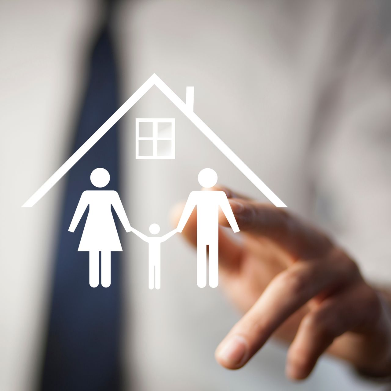 Une main tendue vers une icône de maison blanche avec une silhouette familiale à l’intérieur, sur fond flou.