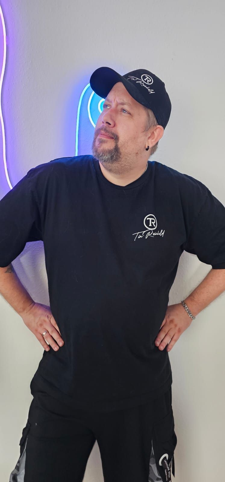 Ein Mann mit schwarzem Hut und schwarzem T-Shirt hat die Hände in die Hüften gestemmt